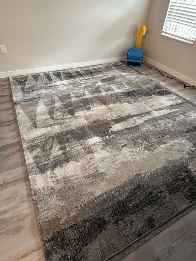 A gray abstract area rug on a wood floor drying under a yellow air mover