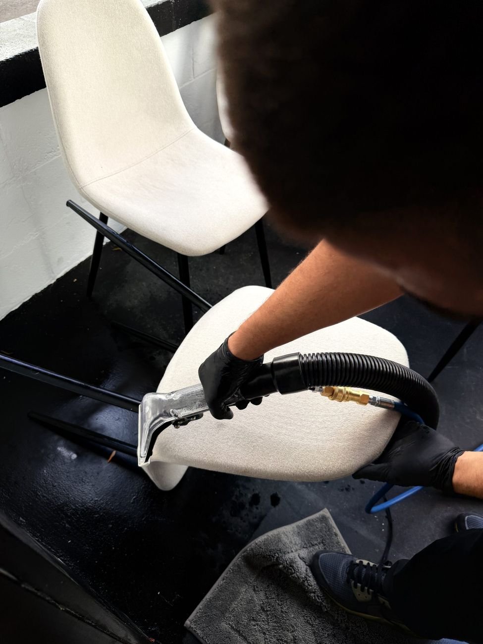 An extraction wand cleaning a white upholstered dining chair