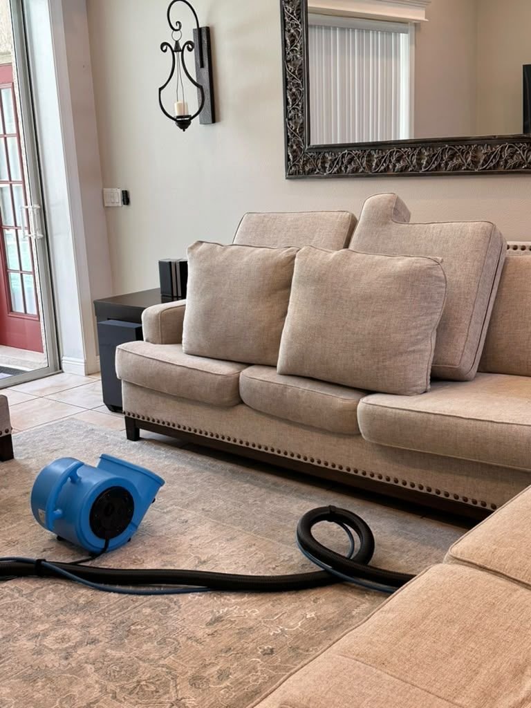 A beige sofa with its cushions standing up to dry beside a blue air mover