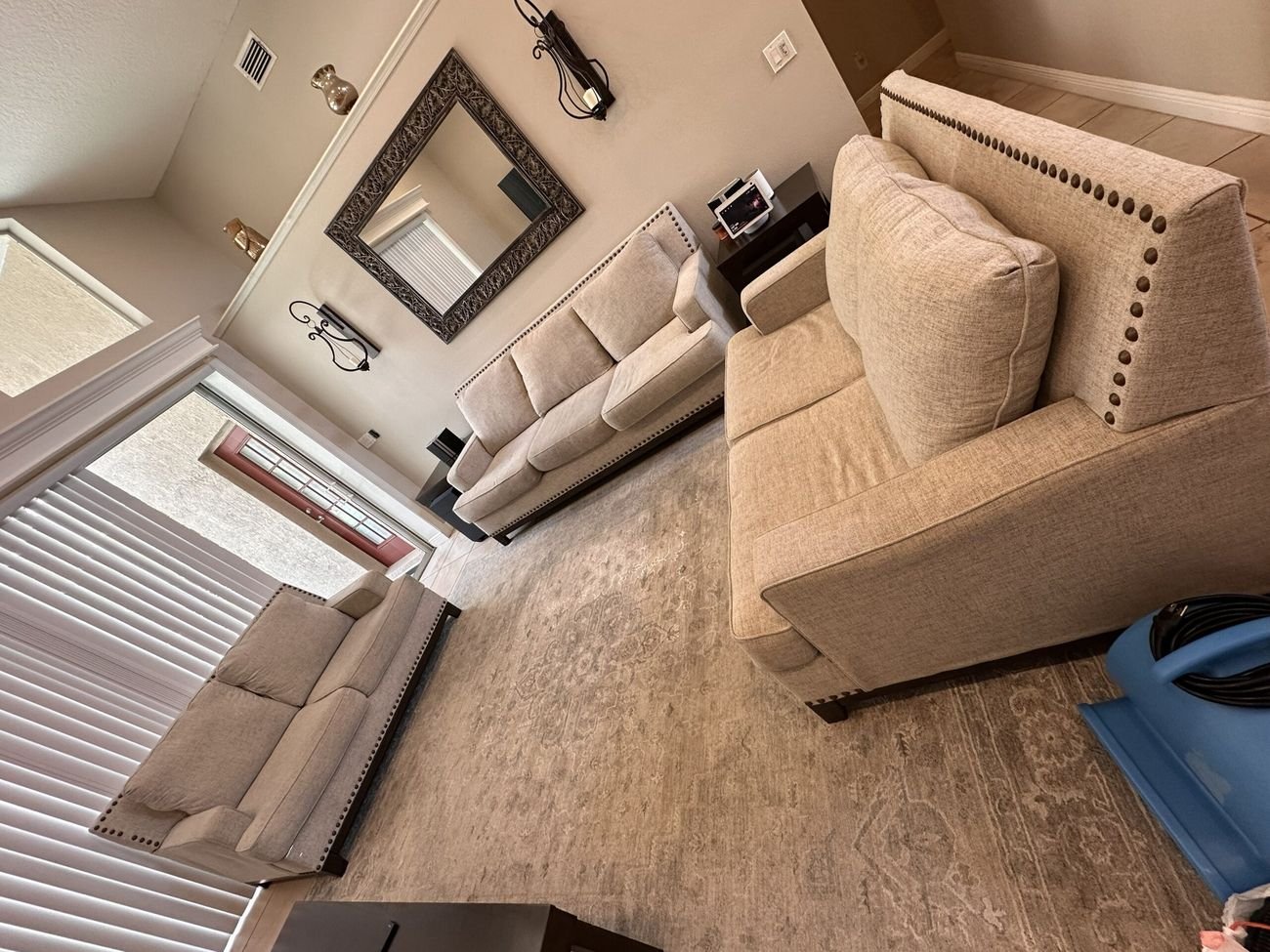 A beige nailhead sofa set in a living room with a blue air mover on the floor